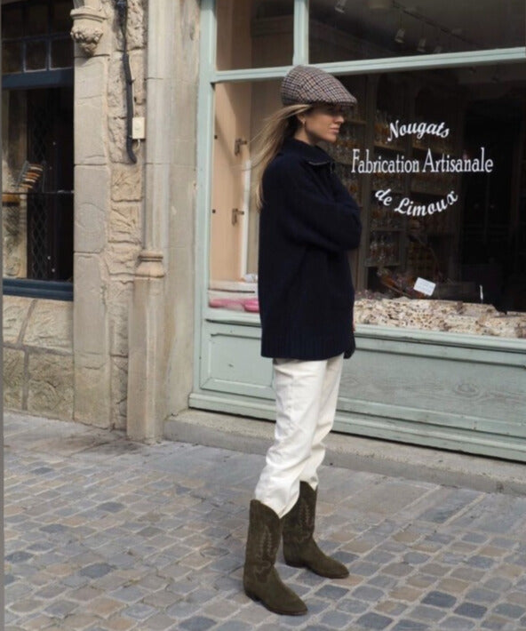 Jeune femme portant Shiloh Heritage,Bottes Midnight, santiag en daim, couleur olive, fabrication artisanal, cuir d’Italie. Robe noire courte et veste en jean. Young woman wearing Shiloh Heritage, Midnight boots, Western boots, Cowboy Boots in suede, color olive, handcrafted ,leather from Italy. Wearing short black dress and jean jacket.